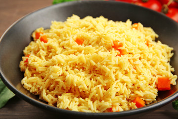 Stewed rice with a carrot on a black plate over wooden background, close up