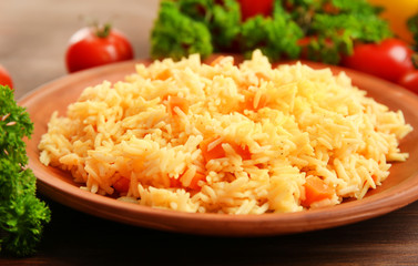 Stewed rice with a carrot on a brown plate over wooden background, close up