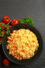 Stewed rice with a carrot and tomatoes on a plate over black background, close up