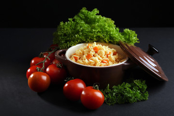 Stewed rice with a carrot and tomatoes in a cooking pot over black background