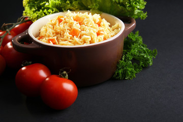 Stewed rice with a carrot and tomatoes in a cooking pot over black background