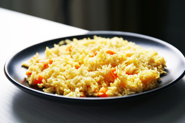 Stewed rice with a carrot on a black plate, close up