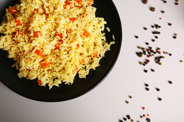 Stewed rice with a carrot on a black plate over white background