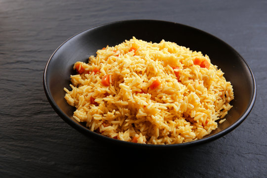 Stewed rice with a carrot on a plate over black background, close up