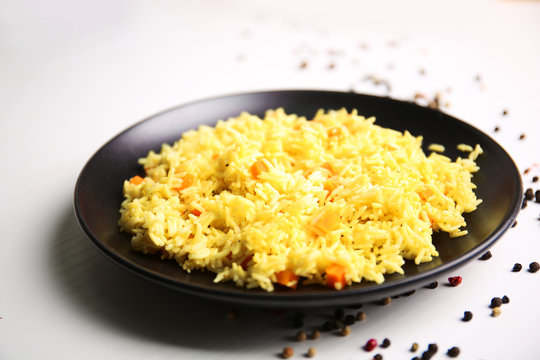 Stewed rice with a carrot on a black plate over white background, close up