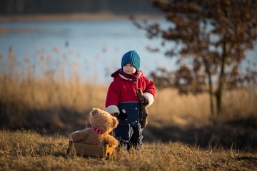 Young happy boy playing outdoor with his teddy bear and trolley