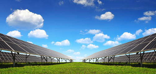 Solar energy panels against blue sky with clouds.