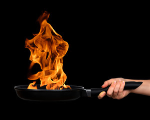 Woman's hand holding a frying pan with flames on black background
