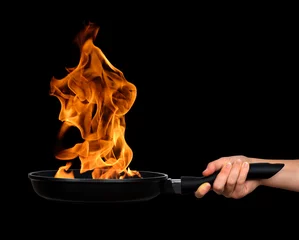  Woman's hand holding a frying pan with flames on black background © vencav