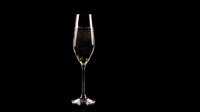flute of champagne with golden bubbles against black background, holiday concept