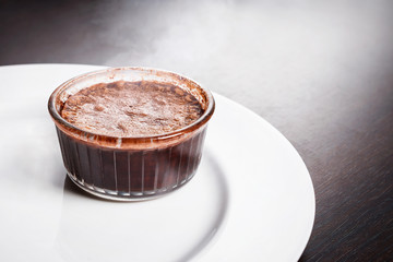 Freshly baked steaming hot dessert chocolate fondant lava cake served on white plate. Famous French dessert on dark wooden table top view.