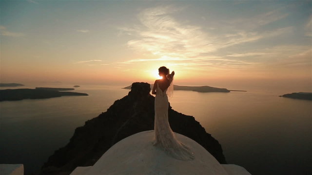 Charming brunette bride enjoying the view on church roof at sunset sky background.