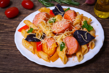 Penne pasta with tomato sauce with sausage, pepper and basil decorated in a plate on a wooden background