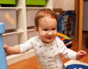 baby standing on his feet in the children's room and smiling