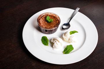 Warm dessert chocolate fondant lava cake served with vanilla ice cream balls and mint on white plate. Famous French dessert on dark wooden table top view