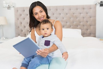 Happy brunette holding her baby and using tablet