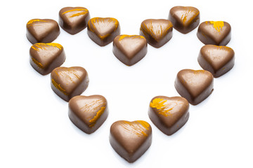 Milk heart shaped chocolates with yellow embellishment arranged in heart on white background from high angle