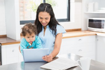 Smiling brunette holding her baby and using tablet