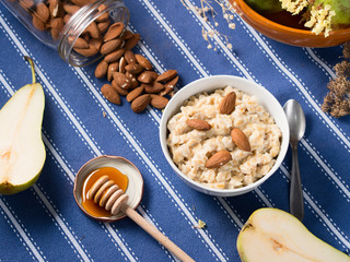 Oatmeal porridge with pears, honey and almonds for breakfast on blue table cloth
