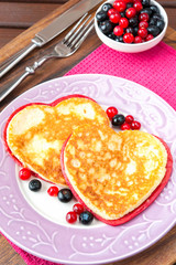 Homemade colored heart shaped pancakes with berries on porcelain plate