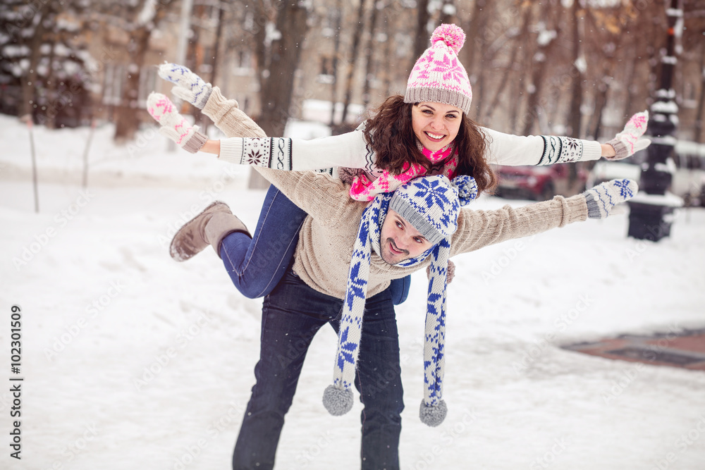 Wall mural Happy young couple walking in winter park piggyback