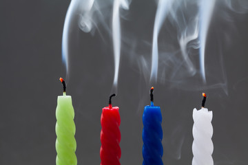 Colorful extinguished candles with white smoke on gray background. four pieces: green, red, blue, white. fading, finishing concept. soft focus macro view