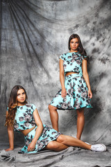 Pretty twins girls in fashion dresses posing over grey background