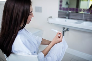 Unhappy woman sitting while looking at pregnancy test
