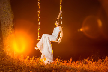 Beautiful happy bride is sitting on swing outddors at sunset