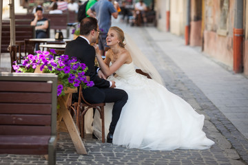 Naklejka premium Cheerful bride and gromm sitting on wooden chairs in french cafe