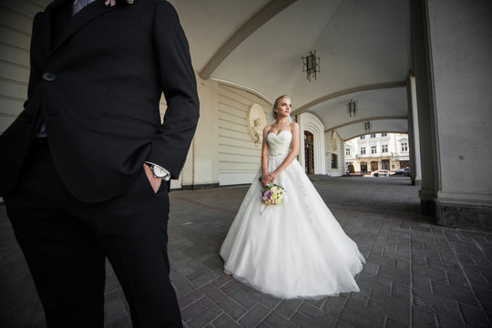 Beautiful blonde bride and groom in black suit posing near old t