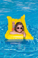 little girl swims in a pool in an yellow life preserver