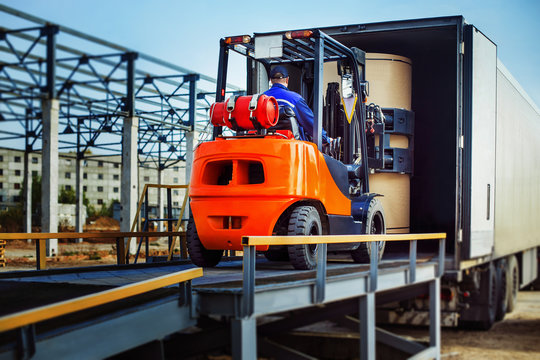 Forklift is putting cargo from warehouse to truck outdoors