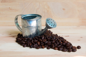 Watering Can miniature and Coffee beans wood background.