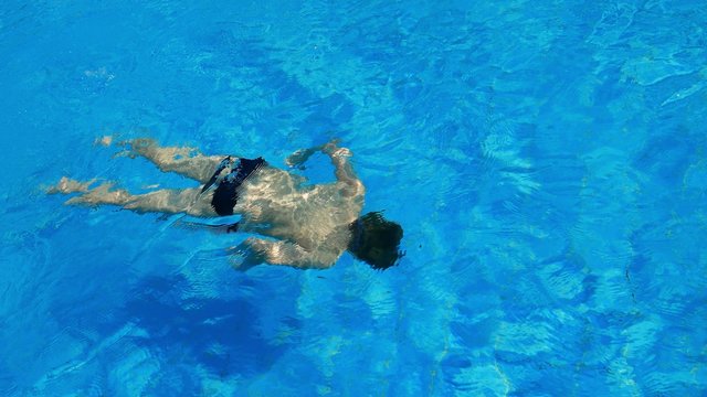 Caucasian child boy teen swimming, dives underwater in outdoor swimming pool . Sun tanning, swimming, tourism, rest and relaxation