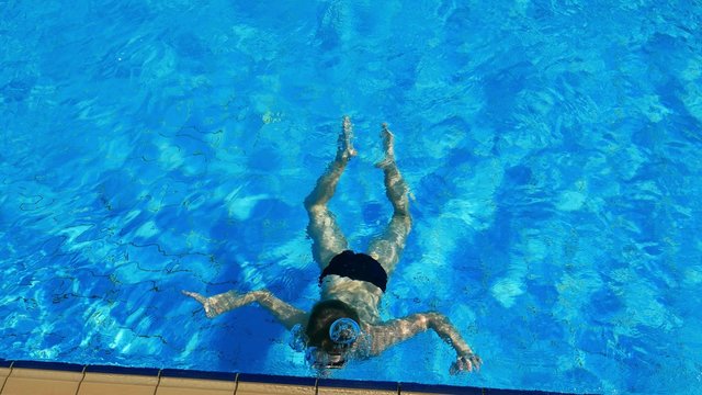 Caucasian child boy teen swimming, dives underwater in outdoor swimming pool . Sun tanning, swimming, tourism, rest and relaxation