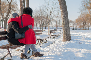 Young couple sitting on bench in park in winter