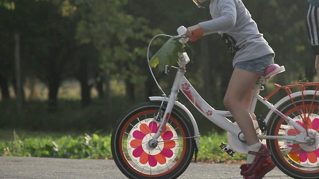 Little girl learning to ride bicycle, afraid to fall down, needs parents' help