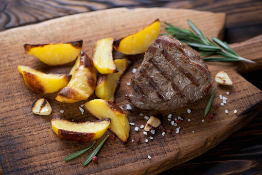 Wooden chopping board with grilled filet mignon steak and potato