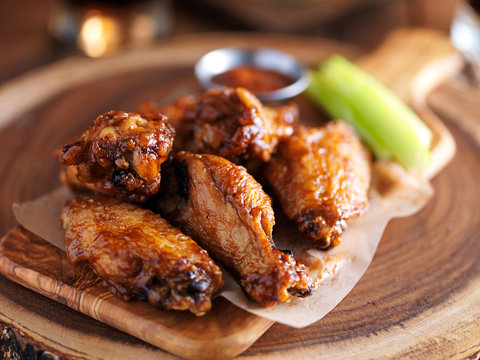 crispy barbecue chicken wings with celery on wooden serving tray