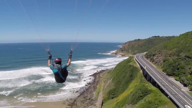POV Paraglider Pilot Chase Cam following behind pilot flying next to a road by the beach in Wilderness, South Africa.