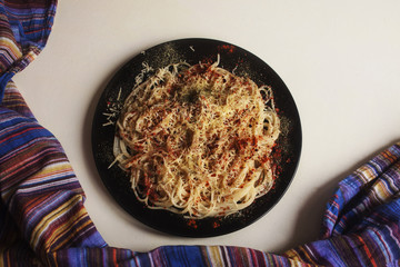 Spaghetti with cheese, paprika and basil on a black plate on white table surrounded by blue fabric