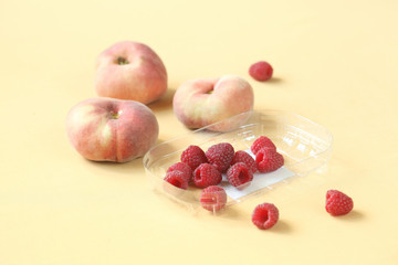 Fresh Donut Peaches and Raspberries on a light yellow background.