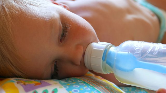 Kid child baby boy drinking milk baby food from a bottle. Childhood dreams and memories.