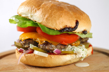 Tasty cheese beef burger with lettuce, cheddar, barbecue sauce, tomatoes, pickles and tzatziki
