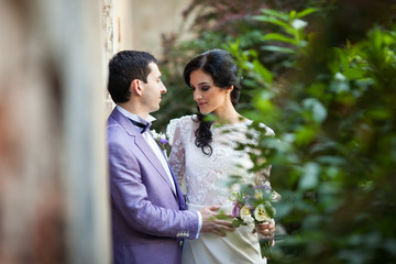 Romantic newlywed couple hugging near old building wall