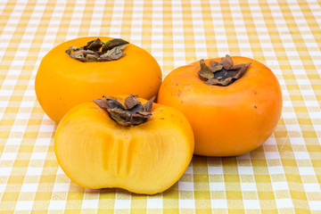 Three ripe persimmons on table. Botanical name of persimmon is Diospyros kaki.