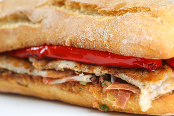 Tasty pork grilled serranito sandwich in a ciabatta with ham and red pepper on a white background