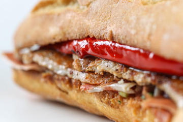 Tasty pork grilled serranito sandwich in a ciabatta with ham and red pepper on a white background