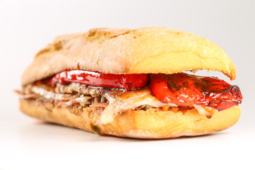 Tasty pork grilled serranito sandwich in a ciabatta with ham and red pepper on a white background